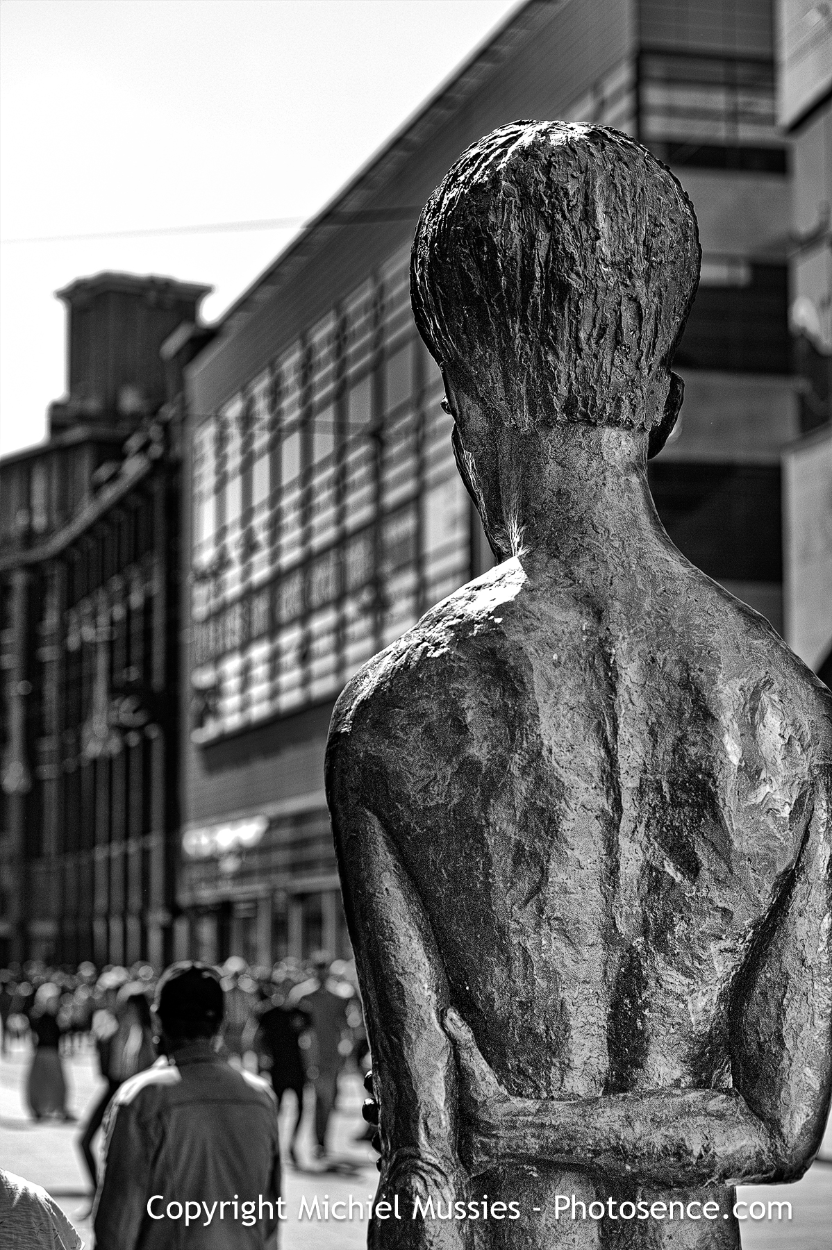 Monochrome print of a statue looking at pedestrian facing the same direction